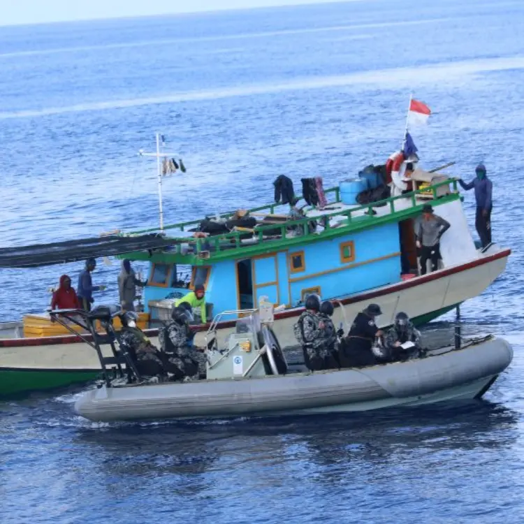 Petugas maritim di perahu karet bermotor naik ke kapal ikan ilegal dengan beberapa nelayan di atasnya